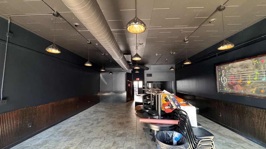 A long restaurant dining room with dark walls and hanging lights