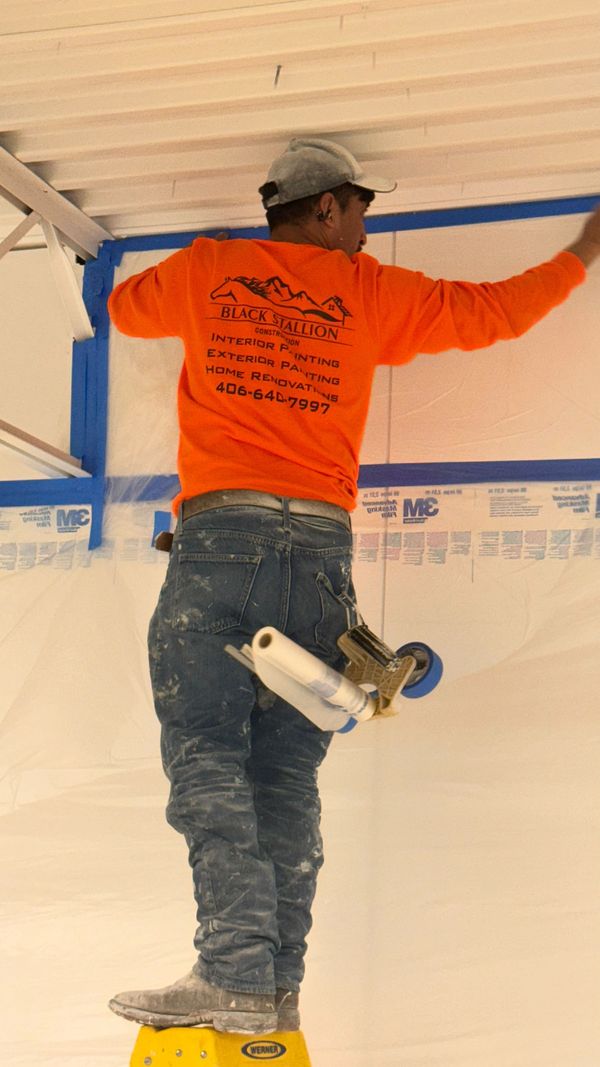 A painter in an orange shirt rolling a ceiling from a ladder