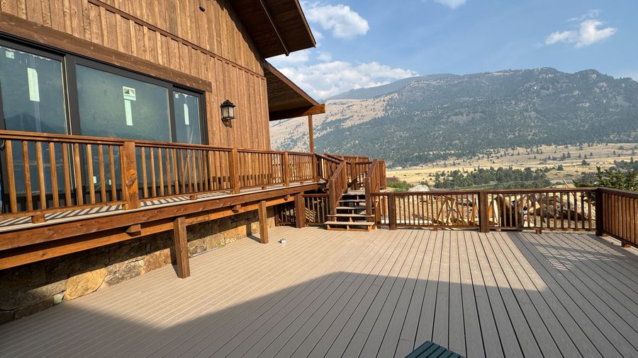 A stained wood deck and railing with mountains in the distance