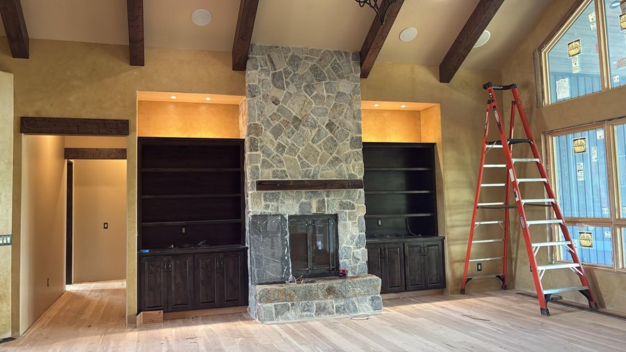 A great room with a stone fireplace, dark built-ins and timber beams