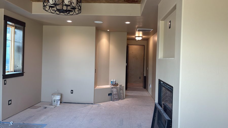 A living room with a fireplace, recessed lighting and a chandelier beyond