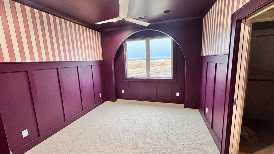 A room with deep plum wainscoting, striped upper walls and an arched window