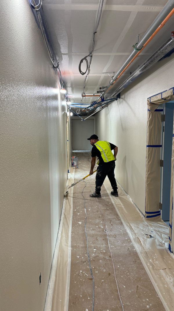 A worker in a high-visibility vest spraying a long corridor