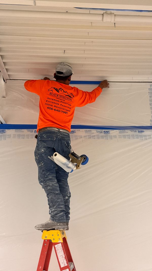 A painter cutting in a ceiling line from a ladder